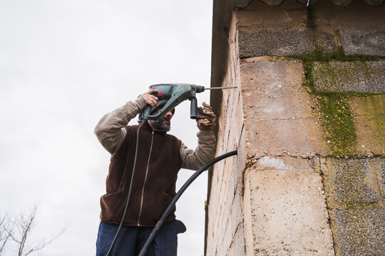 Worker using a rotary hammer drill on a concrete wall