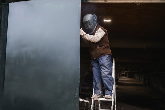 Worker welding metal structure on ladder