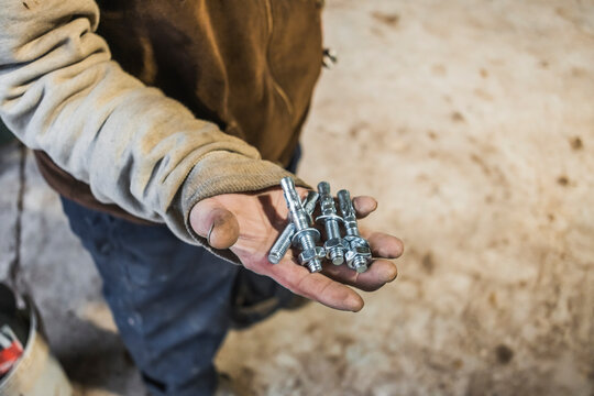 Worker holding metal bolts in dirty hand on site