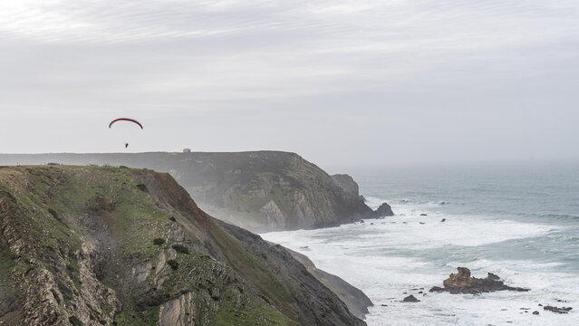 Paraglider over Cordoama cliffs under cloudy skies