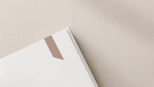 Corner of a white book with a tan bookmark on a beige surface