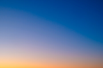 Fototapeta premium Soft gradient sky transitions from deep blue to warm orange. Sunset hues blend seamlessly across the horizon. Ideal for tranquil mood or calming background scenes