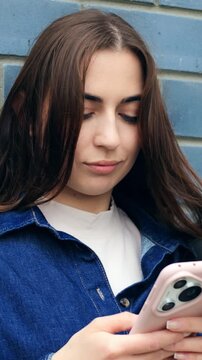 Woman texting outside. Woman engrossed in her phone while standing outside against blue bricks. Female individual diligently typing on her mobile device outdoors with backdrop of blue bricks