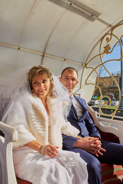 Bride and groom enjoying a romantic ride in a phaeton during their wedding. Portrait of a wedding couple outdoors sitting in an ornate white carriage.