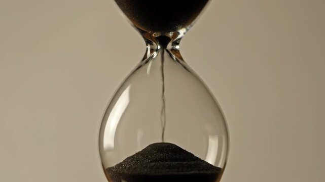 Close up of an hourglass with black sand flowing, concept of passing time and deadlines