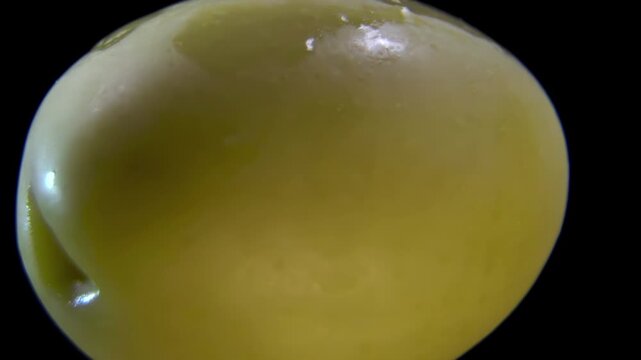 Extreme close-up of pitted green Olive (Olea europaea) coated in brine, glossy epidermis surface, Food Science Background.
