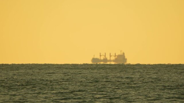 Ship mirage horizon cargo vessel appears as a floating silhouette during sunset creating a fata morgana effect in golden light