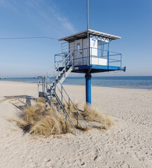 Fototapeta premium A modern blue and white lifeguard rescue station stands prominently on a wide, sandy beach under a clear blue sky