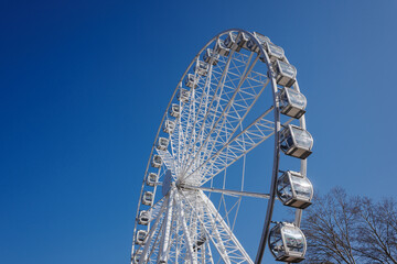 Low-angle view of a large, white modern Ferris wheel with glass gondolas against a deep blue, cloudless sky © Jarama