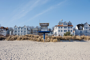 A row of classic white resort architecture and a modern blue lifeguard tower sit behind sand dunes