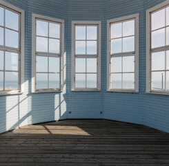 Empty interior of a light blue wooden gazebo featuring large windows with a view of the distant sea horizon