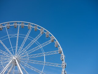 Low-angle view of a large, white modern Ferris wheel with glass gondolas against a deep blue, cloudless sky