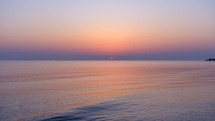 sun sets just above the horizon over a calm Baltic Sea, casting a warm golden-orange glow across the water and sky