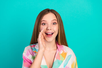 Young woman smiling with a hand gesture against a bright teal background, wearing colorful casual clothing
