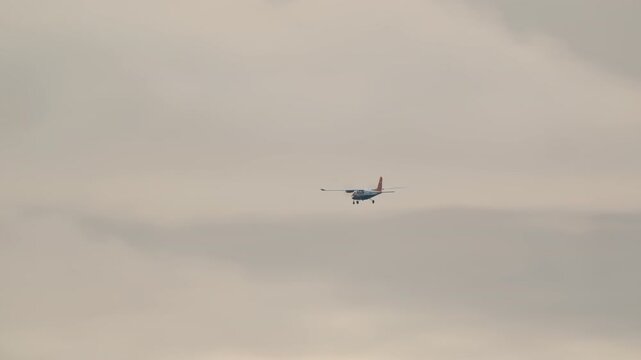 A small twin-engine propeller airplane with landing gear down flies steadily through a vast, overcast sky