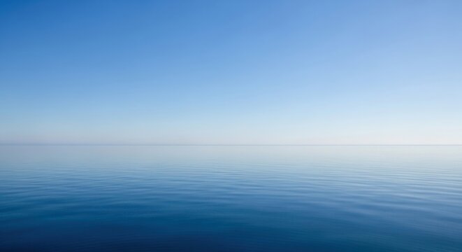 Serene ocean surface stretches towards a clear blue sky, creating a peaceful and unbroken horizon