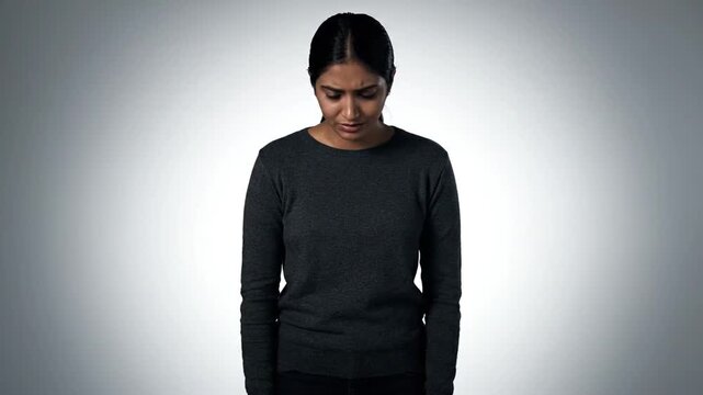 A woman with dark hair wearing a black sweater stands against a plain background, looking downward with a somber or reflective expression. The images are arranged in a grid, capturing her from differ