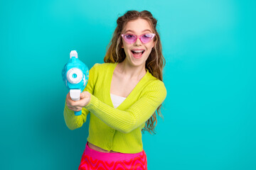 Excited young woman holding a toy water gun on a turquoise background, showcasing fun, style, and cheerful summer vibes