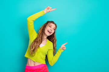 Cheerful young woman in vibrant outfit pointing up against a teal background, embracing positivity and stylish charm