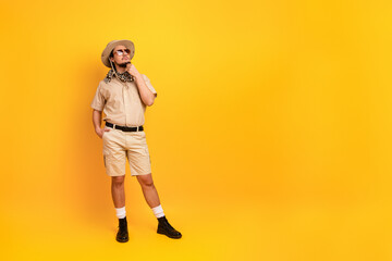 Man in safari outfit stands against a bright yellow backdrop with a thoughtful pose for travel style © deagreez