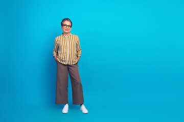 Aged female senior model stands with hands in pockets wearing striped shirt and casual pants...