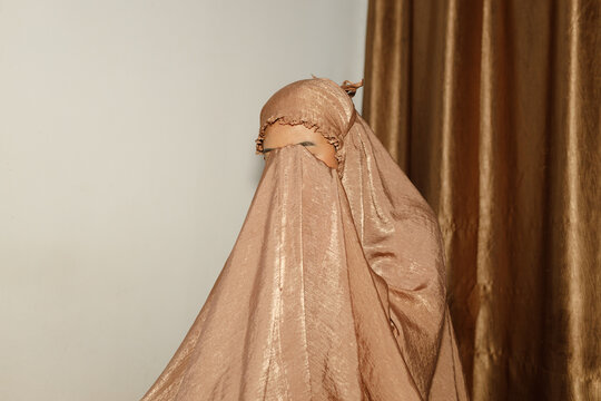 Portrait of Muslim woman wearing mukena covering her face during prayer indoors. Concept of Islamic worship, spirituality, modesty, devotion, and Ramadan reflection