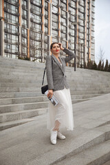 Visionary lady boss in grey jacket and white skirt on stone steps. Successful female specialist with printed media near modern urban area. Business aesthetics and leadership concept.