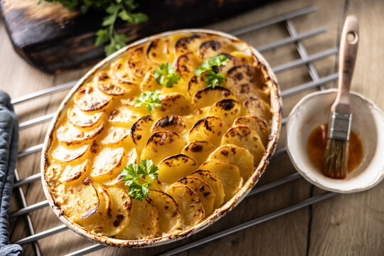 Golden-brown gratin potatoes, neatly arranged in a white ceramic bowl and garnished with fresh herbs. In Slovakia, however, this dish is known primarily at home as French potatoes