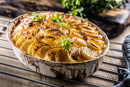 Golden-brown gratin potatoes, neatly arranged in a white ceramic bowl and garnished with fresh herbs. In Slovakia, however, this dish is known primarily at home as French potatoes
