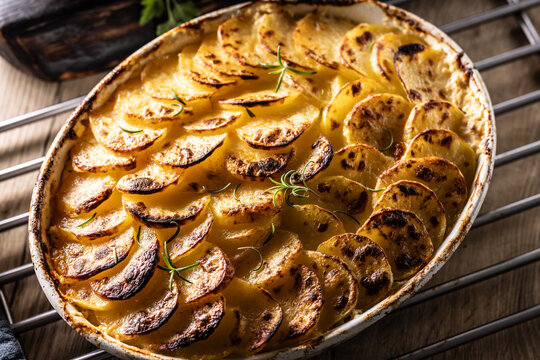 Golden-brown gratin potatoes, neatly arranged in a white ceramic bowl and garnished with fresh herbs. In Slovakia, however, this dish is known primarily at home as French potatoes