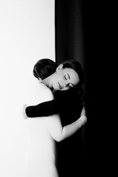 Zwei Frauen in schwarzem und wei&szlig;en Overall umarmen sich vor schwarz-wei&szlig;em Hintergrund