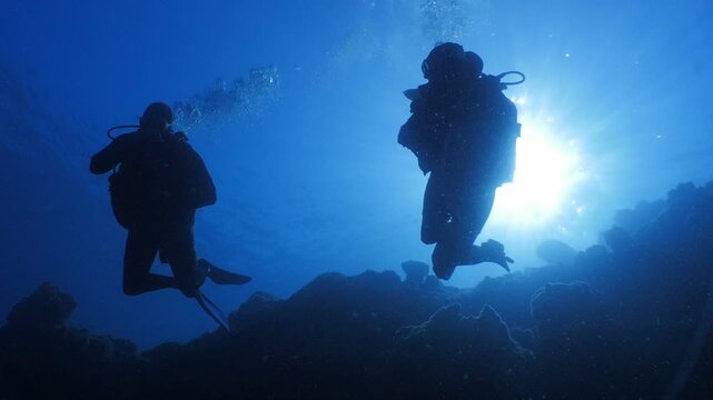 scuba divers exploring underwater with sun beams and rays
