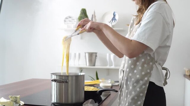 woman takes cooked pasta out of boiling water in pot in the kitchen, girl cooks Italian food on the stove at home