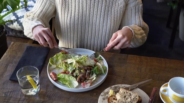 young beautiful woman mixes Caesar salad in cafe, girl with knife and fork eats salad in restaurant