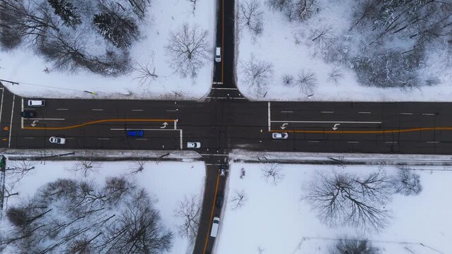 Aerial Drone Above Winter Intersection Snow Plow Traffic. Static 4K perpendicular drone view over regulated intersection with cars and snow plow on snowy winter day. Cleared roads, snow drifts.