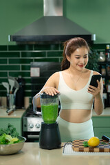 Woman checking smartphone after making green smoothie