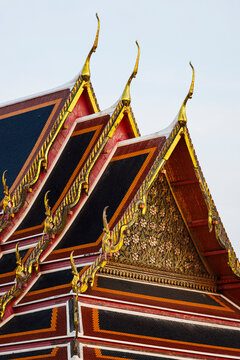 Detail of traditional Thai temple roof featuring golden chofas and ornate floral gable wood carvings in Bangkok, Thailand.