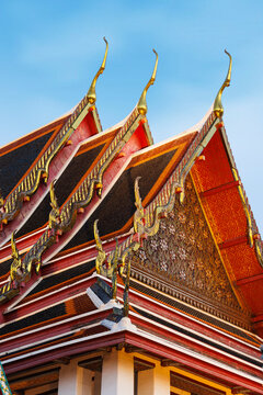 Detailed view of traditional tiered Thai temple roofs featuring golden chofa finials and intricate carvings against a blue sky, Bangkok, Thailand.