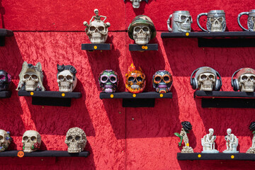 Decorative skull souvenirs displayed on shelves against a red backdrop. © Sergey Kohl