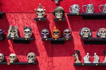 Decorative skull souvenirs displayed on shelves against a red backdrop. © Sergey Kohl