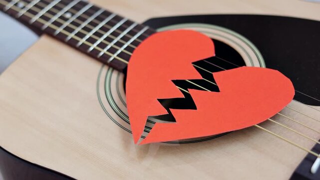Broken red paper heart on acoustic guitar strings. Heartbreak playlist. Concept of heartbreak, emotional pain, breakup.