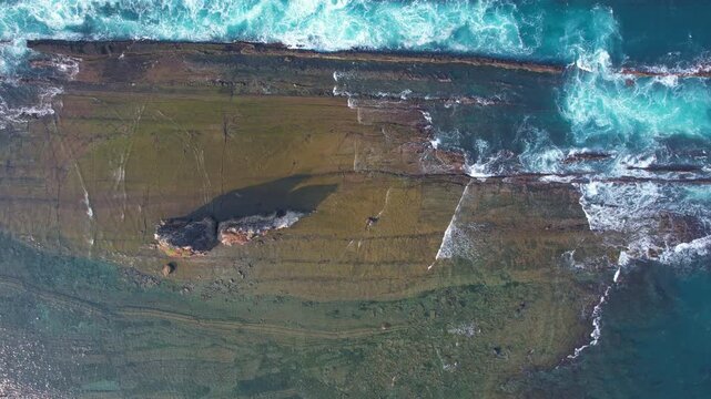 Aerial drone footage from above of the Tanjung Layar pointy rock formation in the middle of the rocky beach, with many waves hitting the reef, in Sawarna, Banten, Java, Indonesia