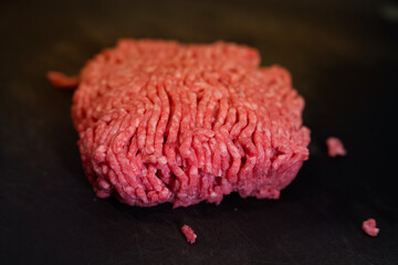 Obraz premium A detailed macro close-up shot of raw ground beef on a dark surface, highlighting the vibrant red color and texture. The shallow depth of field emphasizes the freshness and detail of the meat, perfect