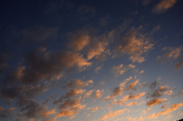 Beautiful sky with soft clouds illuminated by warm sunlight during sunset. The pastel tones of pink, orange, and blue create a calm and dreamy atmosphere — perfect for backgrounds, nature scenes