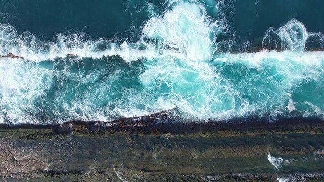 Aerial drone footage from above of Tanjung Layar beach edge, a flat rocky beach, blue sea, with many waves passing the reef, streams like whirlpools, in Sawarna beach, Banten, Java, Indonesia