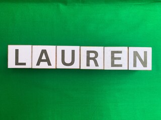 Obraz premium The female first name Lauren spelled out with white alphabet letter tiles on a solid bright green fabric background. Flat lay concept.