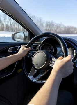 Hands holding a black leather steering wheel of a car, view from the interior onto the road
