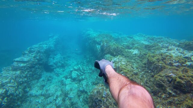 A first-person perspective of a snorkeler's legs and fins gliding over a sunlit volcanic rock trench in the turquoise waters of Pr&iacute;ncipe Island, S&atilde;o Tom&eacute; and Pr&iacute;ncipe.