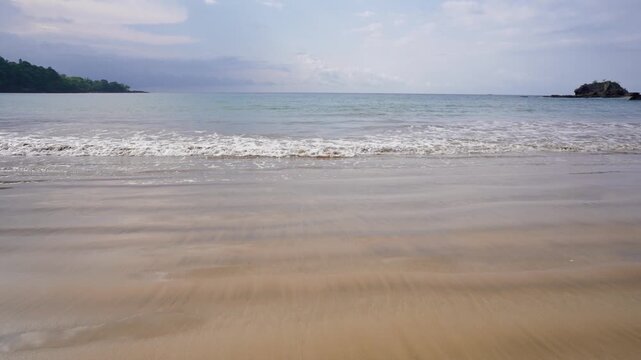 Small waves wash over smooth, wet sand on a secluded tropical beach with a distant forested headland on S&atilde;o Tom&eacute; Island, S&atilde;o Tom&eacute; and Pr&iacute;ncipe.