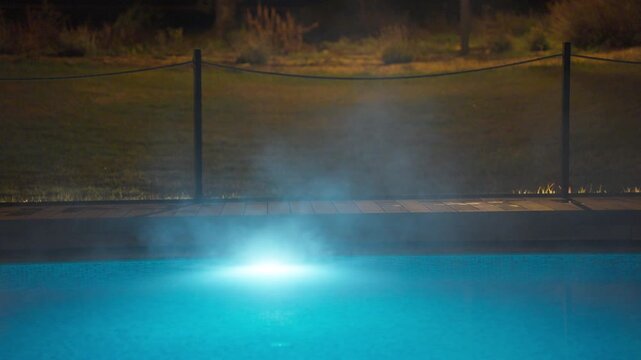 Steaming swimming pool at night, illuminated by a vibrant blue light from below. The ethereal mist rises gracefully, creating a serene and mysterious atmosphere. Perfect for themes of relaxation